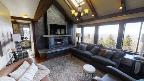 Spacious living area in pedestal house vacation rental featuring a stone fireplace, vaulted ceilings, and panoramic views of the Snowshoe treetops